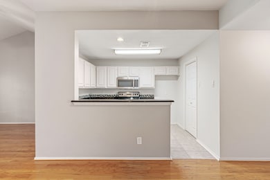 Kitchen featuring electric stove, kitchen peninsula, white cabinets, and light wood-type flooring