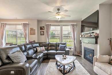 Living room with dark wood finished floors, a tile fireplace, a textured ceiling, and a ceiling fan