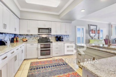 Kitchen with stainless steel appliances, decorative backsplash, crown molding, light stone counters, and white cabinetry