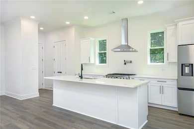 Kitchen with wall chimney range hood, stainless steel fridge with ice dispenser, a center island with sink, dark wood-style flooring, and ornamental molding