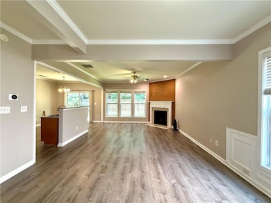 Unfurnished living room featuring wood finished floors, a chandelier, a fireplace with raised hearth, ceiling fan, and crown molding