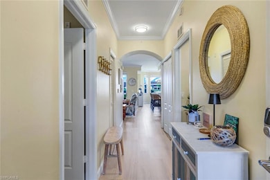 Hall with ornamental molding, light wood-type flooring, arched walkways, and visible vents