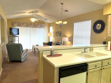 Kitchen featuring ceiling fan with notable chandelier, dishwasher, lofted ceiling, sink, and light carpet