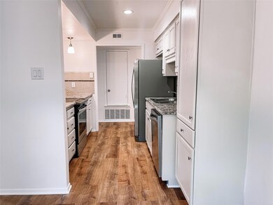 Kitchen featuring decorative light fixtures, white cabinetry, stainless steel appliances, crown molding, and light wood-type flooring