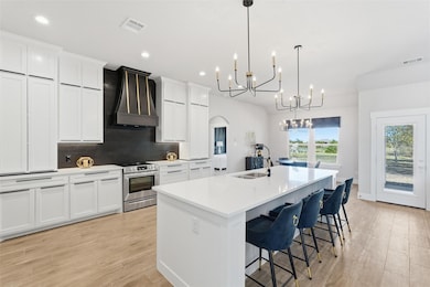 Kitchen with arched walkways, tasteful backsplash, custom exhaust hood, white cabinetry, and recessed lighting