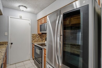 Kitchen featuring stainless steel appliances, a textured ceiling, tasteful backsplash, light tile patterned floors, and light stone counters