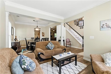 Living area with decorative columns, wood finished floors, stairs, and crown molding