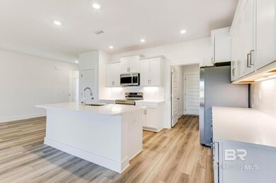 Kitchen with white cabinets, backsplash, stainless steel appliances, light hardwood / wood-style floors, and a center island with sink