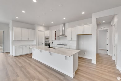 Kitchen with white cabinets, a kitchen bar, a center island with sink, light wood-style floors, and light stone countertops