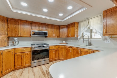 Kitchen featuring a tray ceiling, recessed lighting, brown cabinetry, stainless steel appliances, and light wood-type flooring