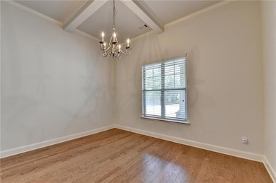 Spare room featuring wood finished floors, beam ceiling, a chandelier, and ornamental molding
