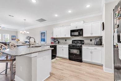Kitchen with black appliances, a sink, a kitchen bar, white cabinetry, and decorative backsplash