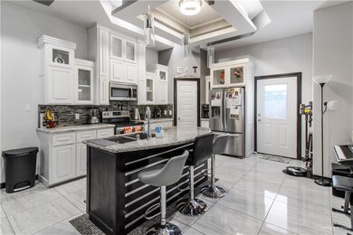Kitchen featuring light stone countertops, a center island with sink, appliances with stainless steel finishes, and white cabinets