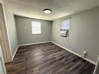Empty room with a textured ceiling, cooling unit, dark wood-style flooring, and baseboards