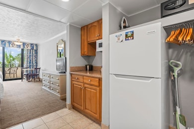Kitchen with white appliances, brown cabinetry, crown molding, light tile patterned floors, and light countertops