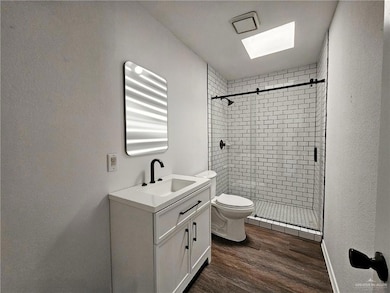 Full bathroom featuring vanity, a shower stall, wood finished floors, a skylight, and a textured wall