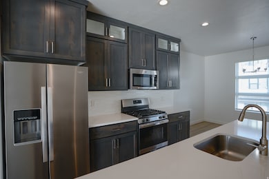Kitchen featuring appliances with stainless steel finishes, decorative light fixtures, glass insert cabinets, decorative backsplash, and light stone countertops