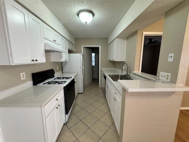 Kitchen featuring range with gas cooktop, white cabinets, a textured ceiling, under cabinet range hood, and light tile patterned floors