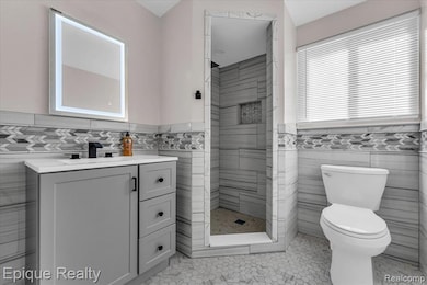 Bathroom featuring tile walls, a wainscoted wall, vanity, a shower stall, and light tile patterned flooring