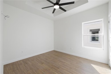 Unfurnished room featuring a raised ceiling, wood finished floors, and a ceiling fan