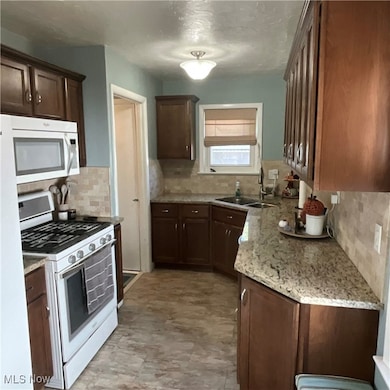 Kitchen with white appliances, light stone counters, decorative backsplash, and dark brown cabinetry