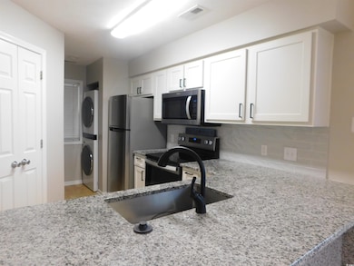 Kitchen featuring range with electric cooktop, light stone counters, white cabinets, stacked washer / dryer, and stainless steel microwave