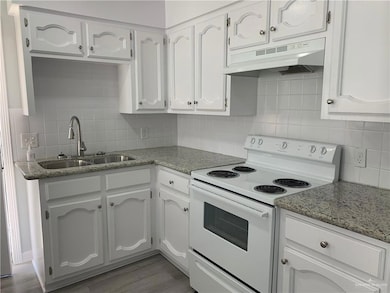 Kitchen with white range with electric cooktop, decorative backsplash, under cabinet range hood, and white cabinets