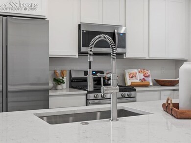 Kitchen with appliances with stainless steel finishes, white cabinetry, and light stone countertops