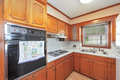 Kitchen with stainless steel electric stovetop, crown molding, black oven, a sink, and backsplash