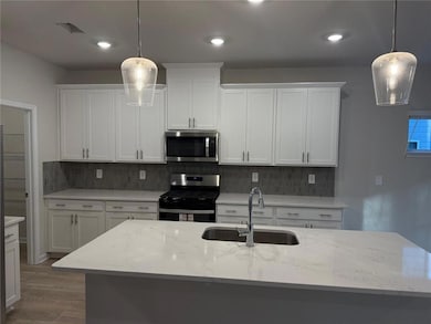 Kitchen with stainless steel appliances, white cabinetry, backsplash, light stone countertops, and recessed lighting