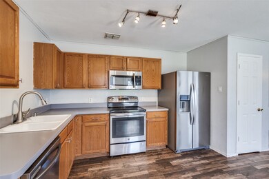 Kitchen with stainless steel appliances, brown cabinetry, dark wood finished floors, and light countertops
