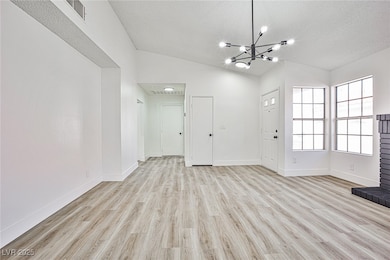 Unfurnished living room featuring light wood-type flooring, a chandelier, lofted ceiling, and a textured ceiling