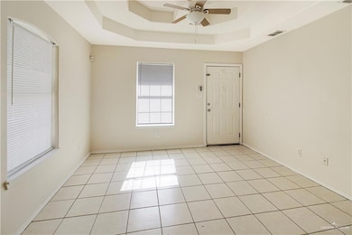 Tiled empty room featuring ceiling fan and a tray ceiling