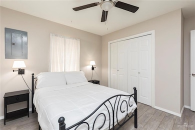 Bedroom with light wood-type flooring, baseboards, a ceiling fan, a closet, and electric panel