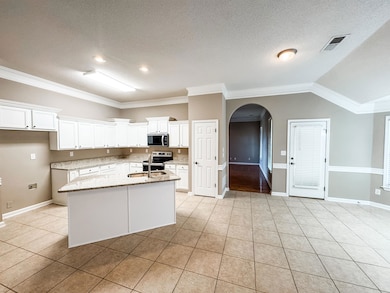 Kitchen featuring stainless steel appliances, arched walkways, light tile patterned floors, crown molding, and white cabinetry