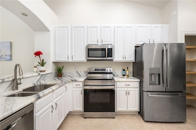 Kitchen featuring stainless steel appliances, white cabinets, light tile patterned floors, and light stone countertops