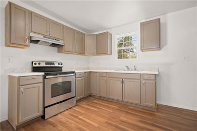 Kitchen featuring stainless steel range with electric stovetop, under cabinet range hood, light wood finished floors, and light countertops