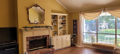 Den area featuring dark wood-style flooring, lofted ceiling, a brick fireplace, and ornamental molding