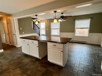 Kitchen with white cabinets, dark countertops, a wainscoted wall, baseboard heating, and a decorative wall