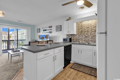 Kitchen featuring backsplash, a peninsula, dark countertops, freestanding refrigerator, and dishwasher