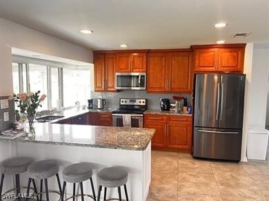 Kitchen featuring stone countertops, kitchen peninsula, appliances with stainless steel finishes, a breakfast bar area, and light tile patterned floors