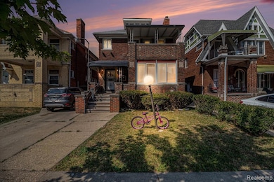 American foursquare style home featuring brick siding, a front yard, a balcony, and a chimney