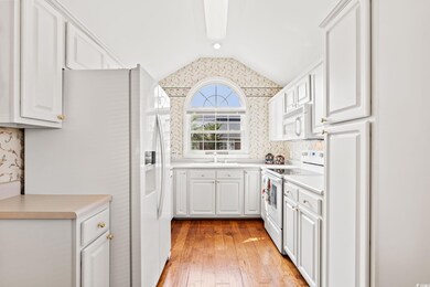 Kitchen with white appliances, lofted ceiling, white cabinets, light wood-style floors, and light countertops