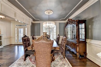 Dining area featuring a chandelier, a decorative wall, wainscoting, dark wood-type flooring, and ornamental molding