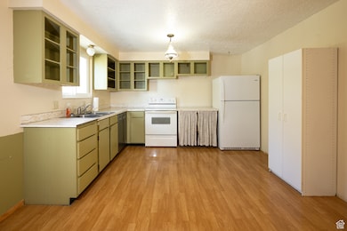 Kitchen featuring white appliances, light countertops, light wood-type flooring, a textured ceiling, and green cabinetry