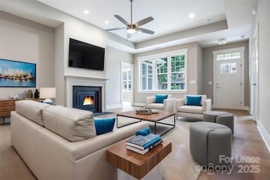 Virtually staged living room with gas fireplace, tray ceiling and ceiling fan.