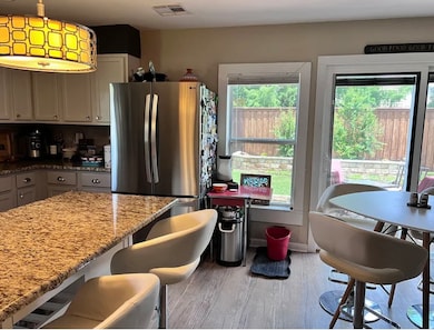 Kitchen with gray cabinets, freestanding refrigerator, light stone countertops, dark wood finished floors, and a kitchen bar