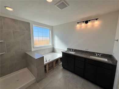 Bathroom featuring double vanity, a textured ceiling, a bath, and light tile patterned floors