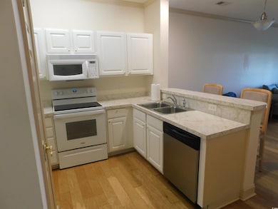Kitchen featuring white appliances, light wood-type flooring, light countertops, a peninsula, and white cabinets