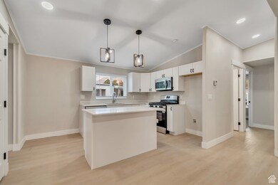 Kitchen featuring white cabinets, a kitchen island, stainless steel appliances, hanging light fixtures, and light wood-style flooring